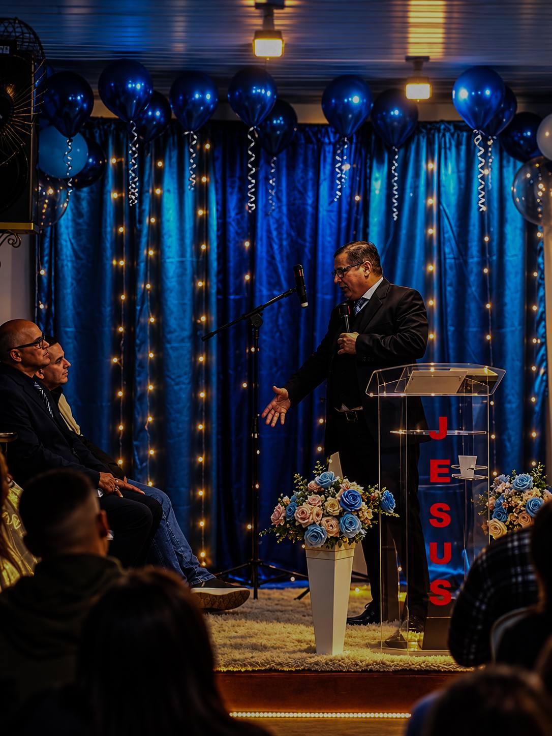 Pregação em um culto da IJC, com o púlpito e cortinas azuis iluminadas